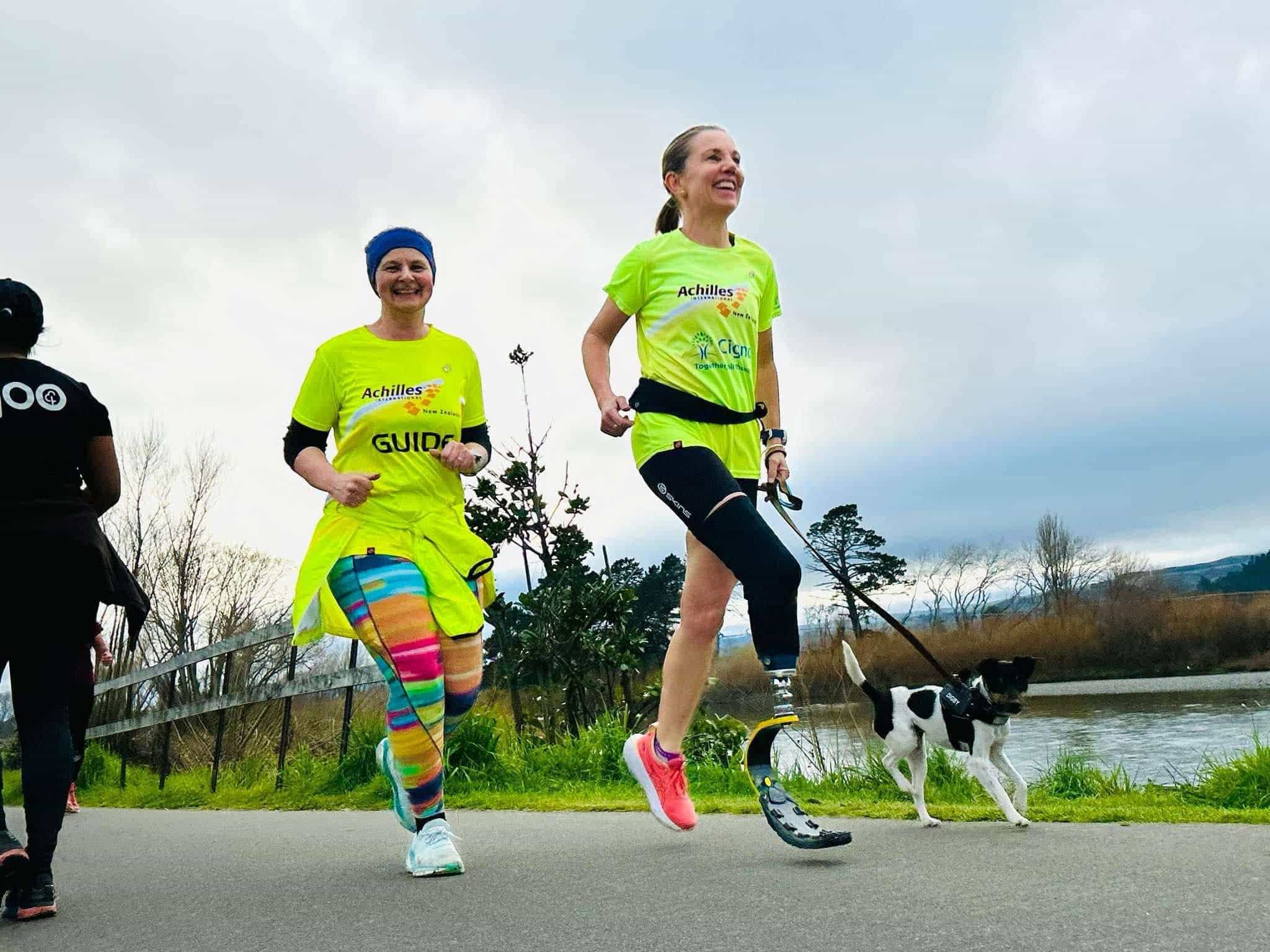 Athlete with a blade and dog running side by side with guide along path alongside river