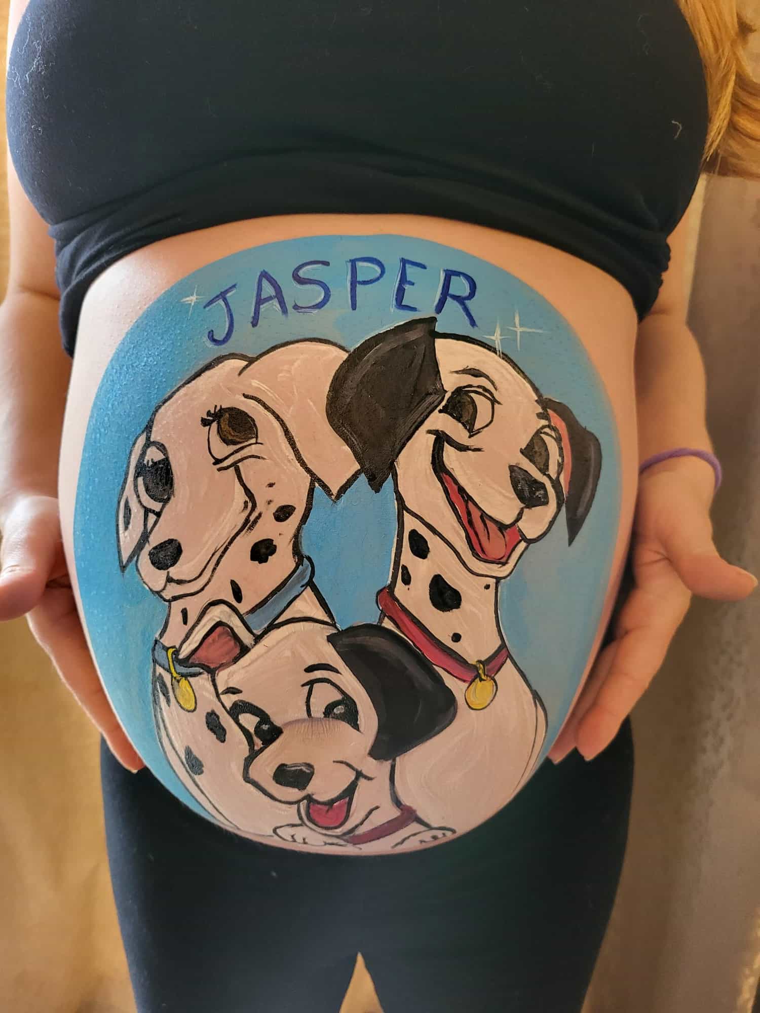 A close up of a baby bump with three dalmations (the parents and a puppy from 101 Dalmations) against a blue background with 'Jasper' painted across the top. 