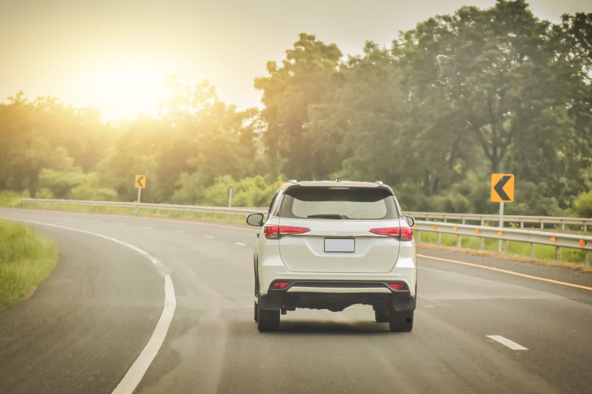 A white car driving around a corner into a setting sun. 