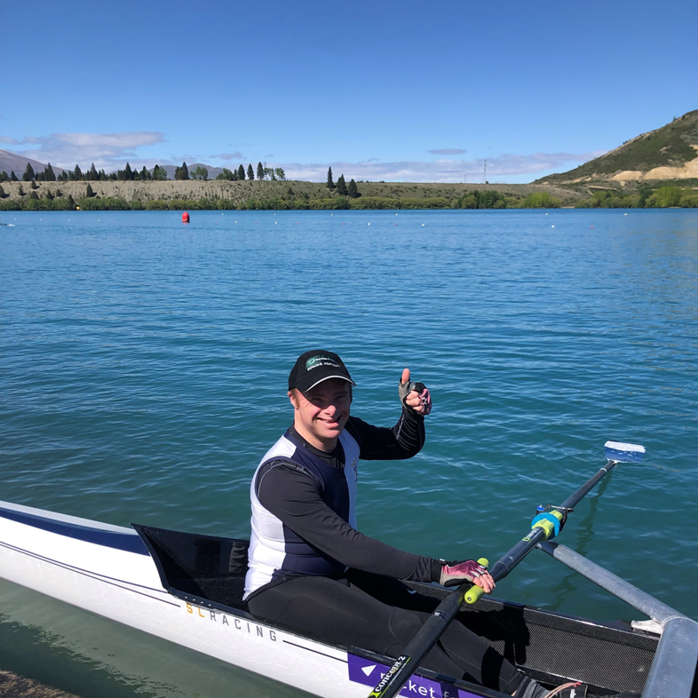 a man smiling on while rowing on a lake.