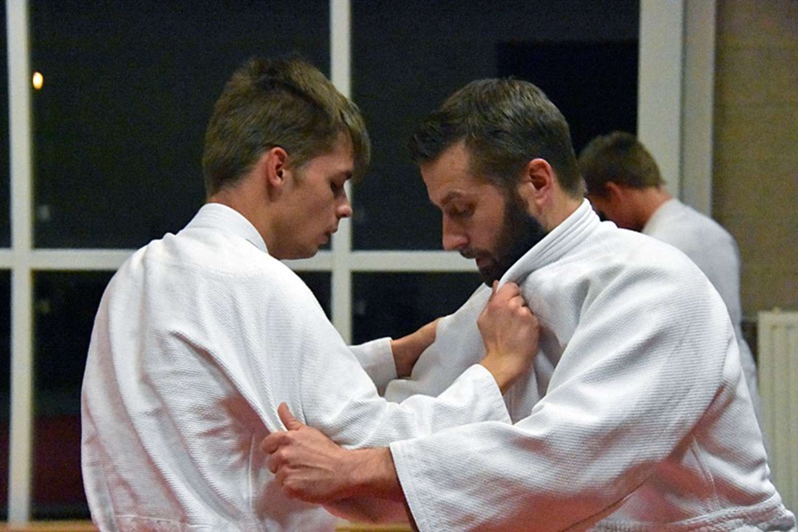 two men in the starting position for judo, where they grip each others uniform before start. 