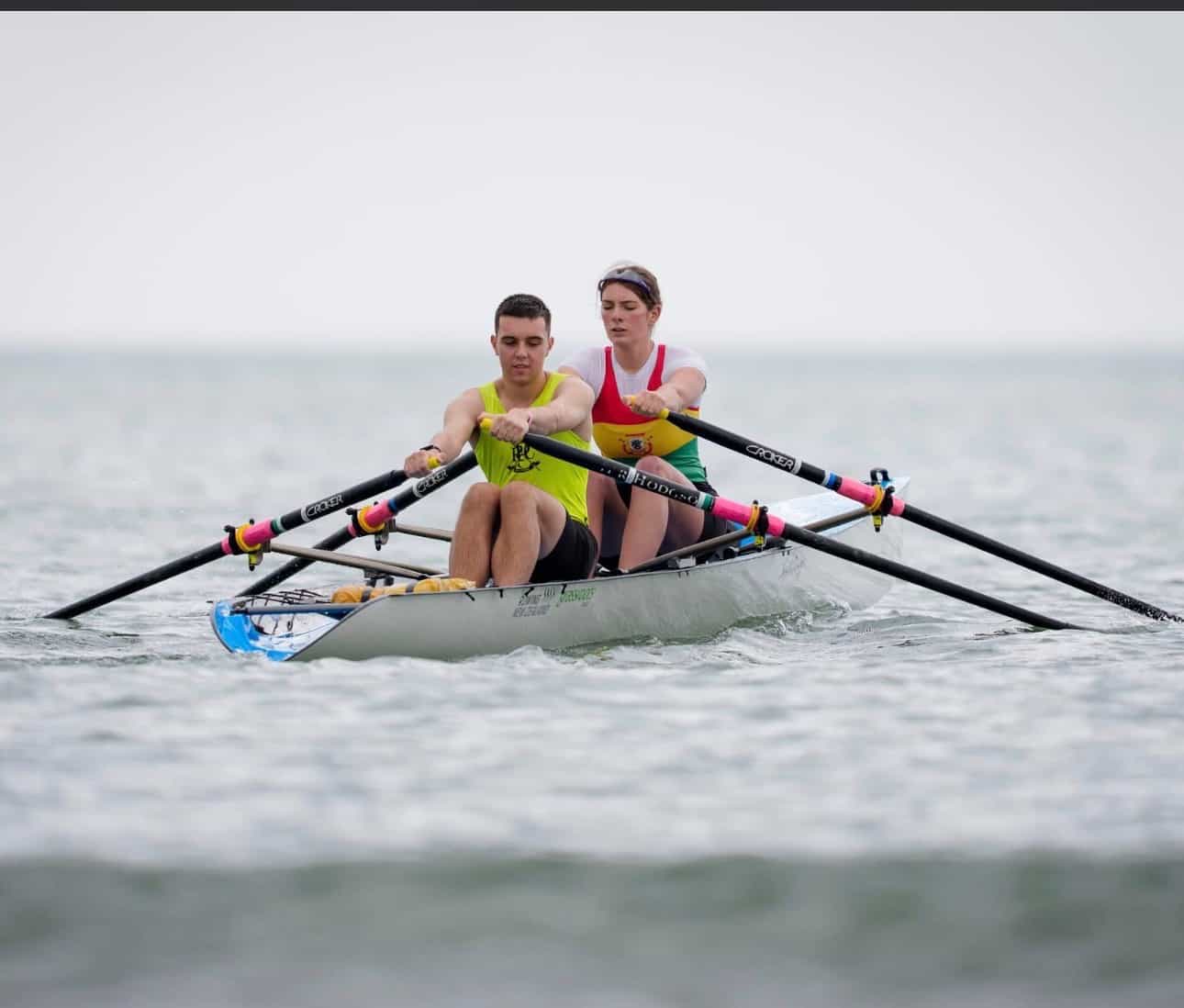 Toby and Amber are rowing as a pair together on a white row boat. 