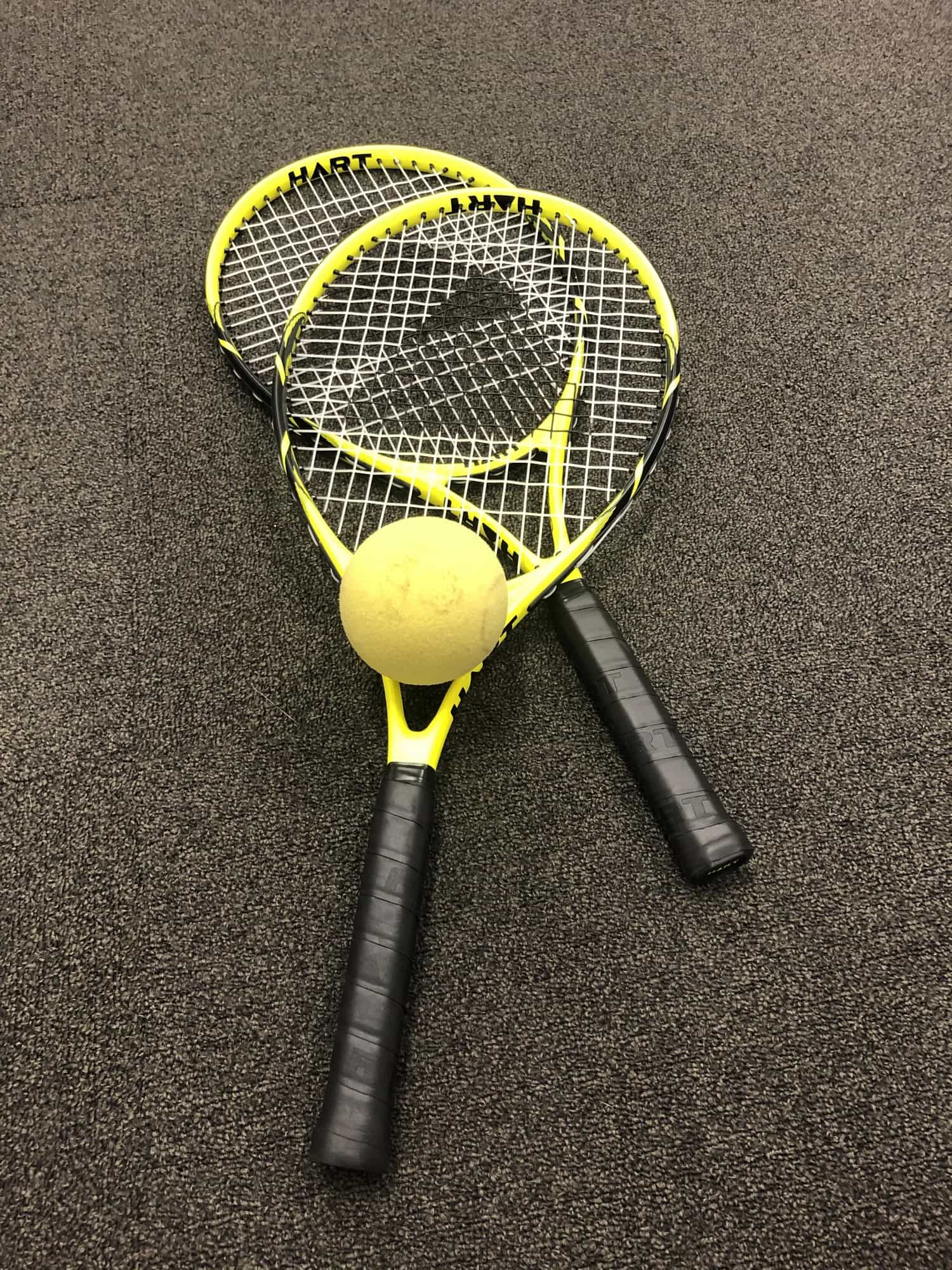 Two tennis racquets on carpet with a foam yellow blind tennis ball