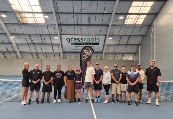 Chelsea from Blind Sport NZ with Ali from Tennis NZ and a number of coaches who have just completed Blind Low Vision Tennis coaching. They are standing at the indoor tennis courts in Albany Tennis NZ headquarters.